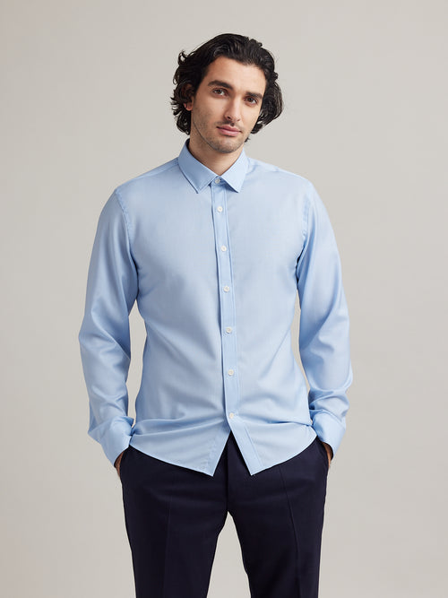Man wears a light blue merino wool shirt in 100% superfine merino wool. 