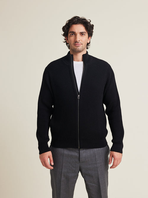 L’homme porte un cardigan en laine mérinos entièrement zippé de couleur noire et des poches latérales de Wolk